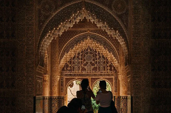 Two figures in silhouette inside a carved stucco window looking out over Granada