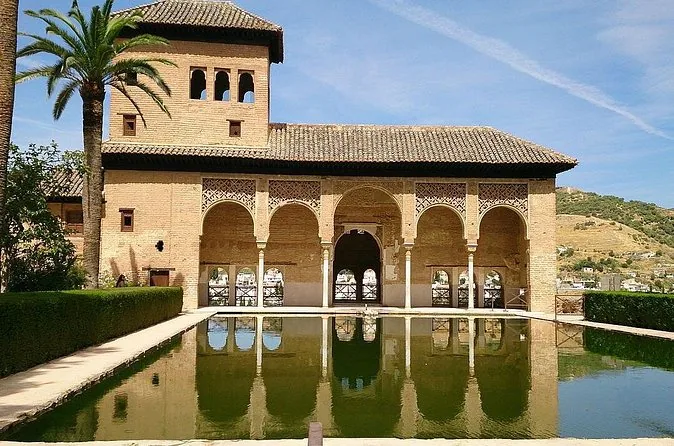 The Partal pavilion with its arcade reflected in a pool, palm trees beside it